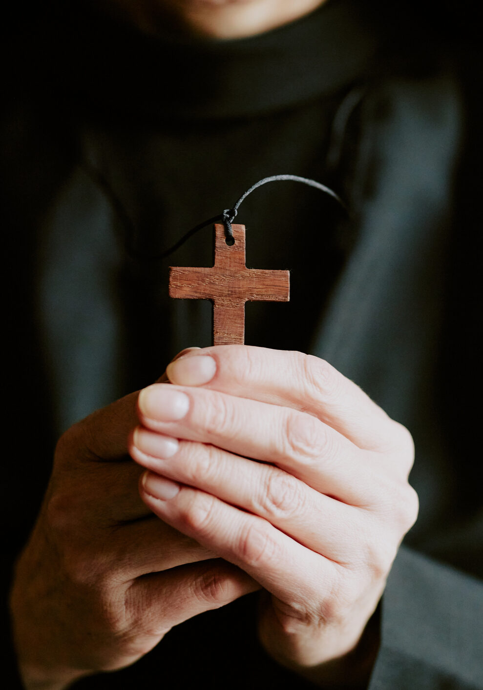 Closeup shot of hands of unrecognizable mature Catholic nun wearing black habit holding wooden cross